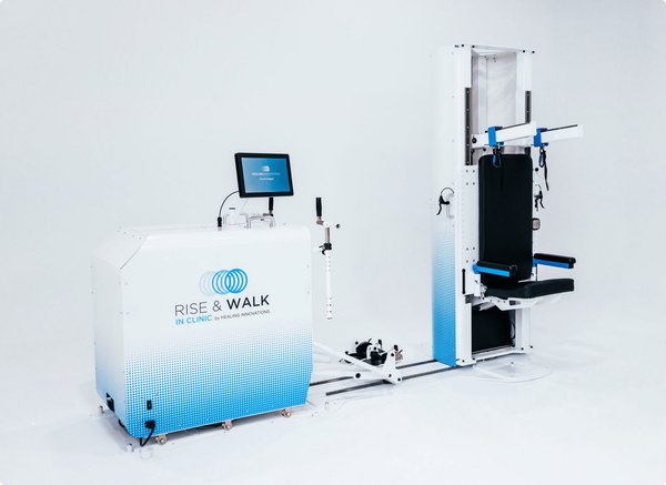 Two-part robotic system on a floor track: a wheeled control cabinet with a touchscreen, and an upright frame with a padded seat, chest and arm supports, and harness straps that raise a seated user to standing.